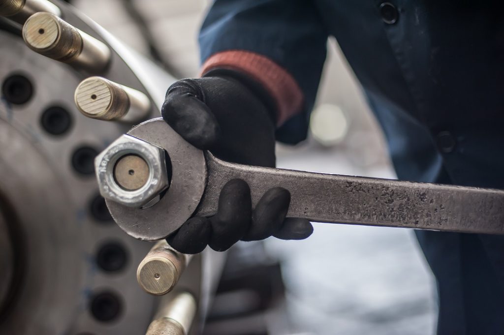 Man working on mechanical repair on factory screws big bolt with large and heavy wrench key