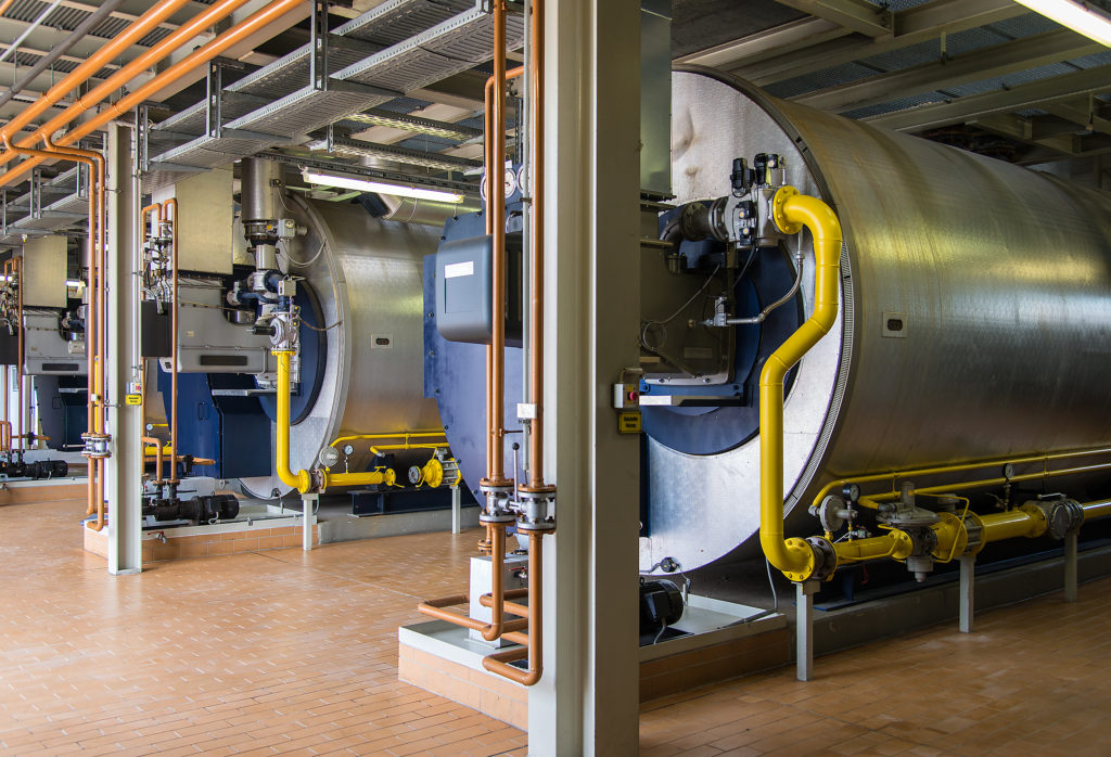 Still of a room of large combustion boilers. 